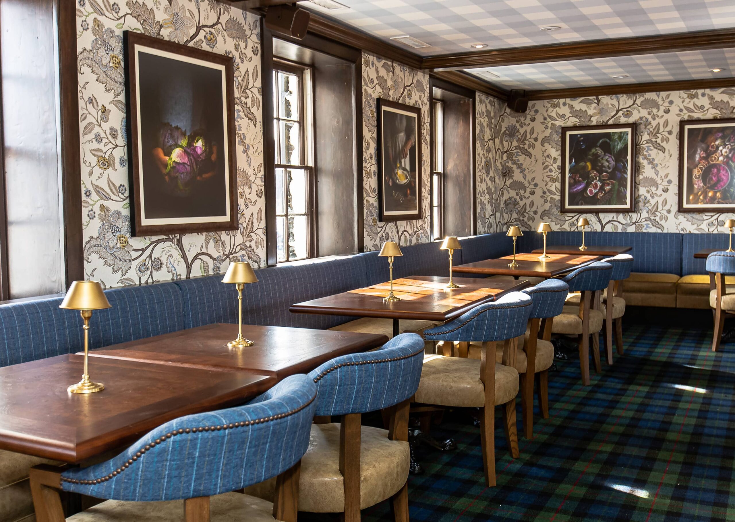 Elegant dining room with floral wallpaper, wooden tables, blue upholstered seating, and wall-mounted lamps.