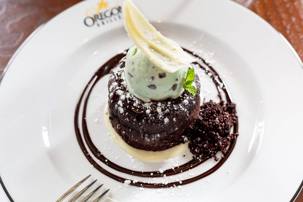A chocolate lava cake served with a scoop of mint ice cream and garnished with powdered sugar on a white plate.