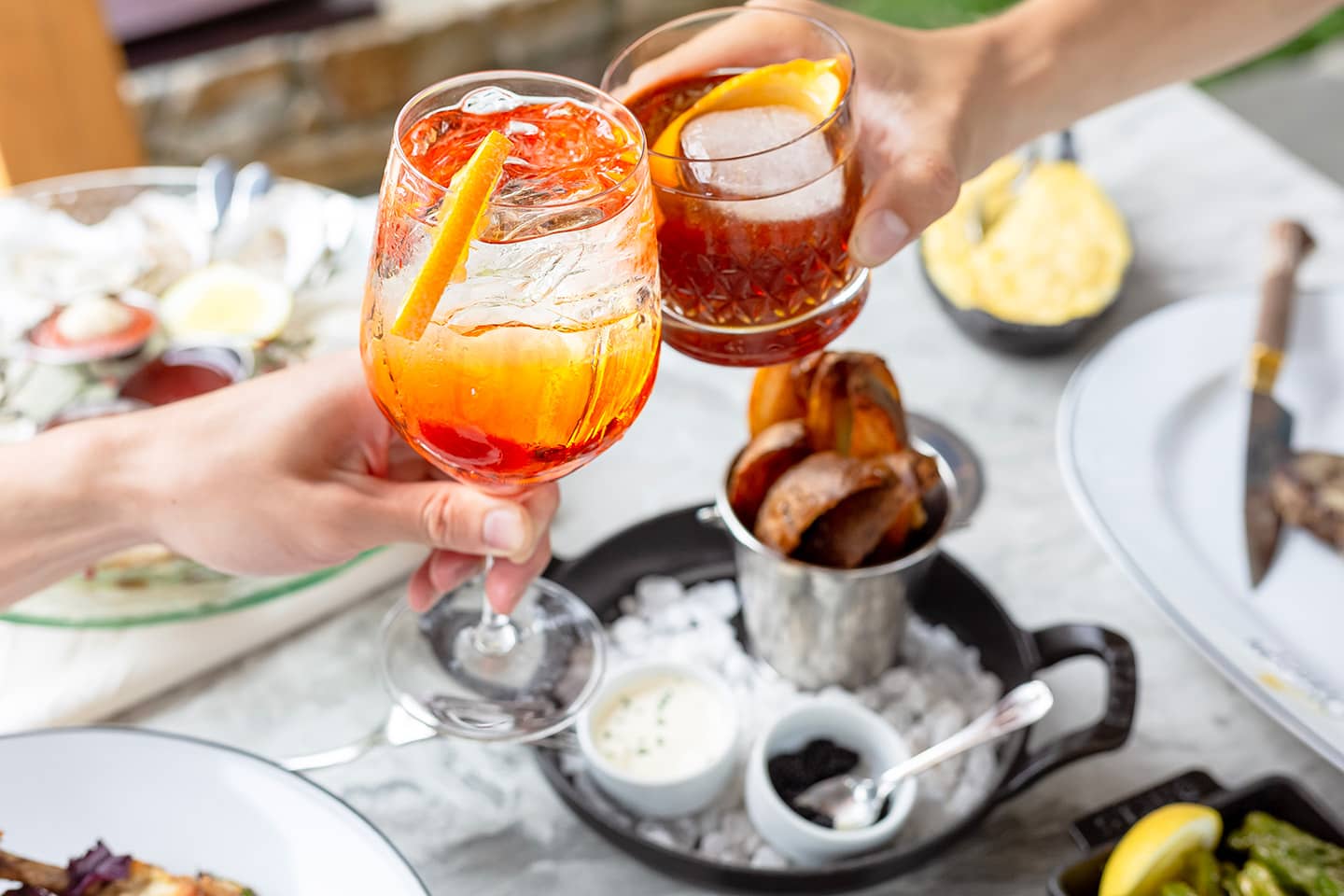 Two people toasting with aperol spritz drinks at a dining table.