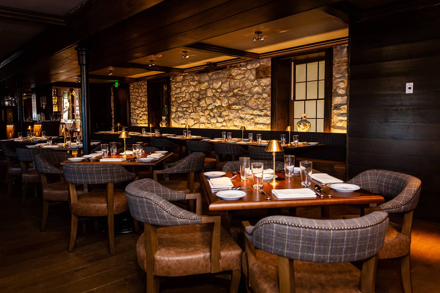 Elegantly set tables in a dimly lit upscale restaurant with stone wall accents.