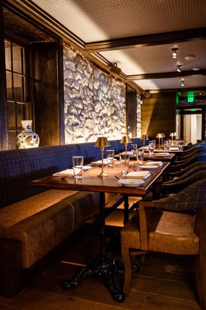 An elegant restaurant setting with set tables and upholstered benches along a stone wall.