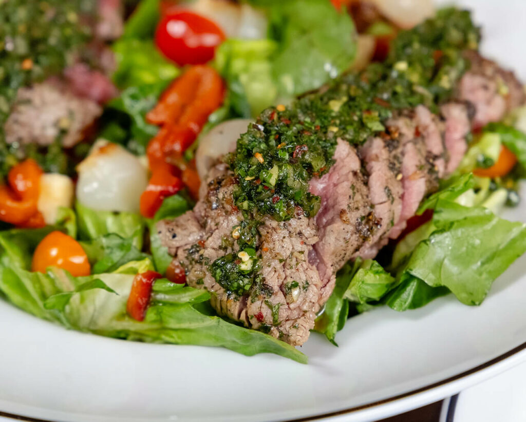 Grilled steak topped with chimichurri on a bed of fresh salad.