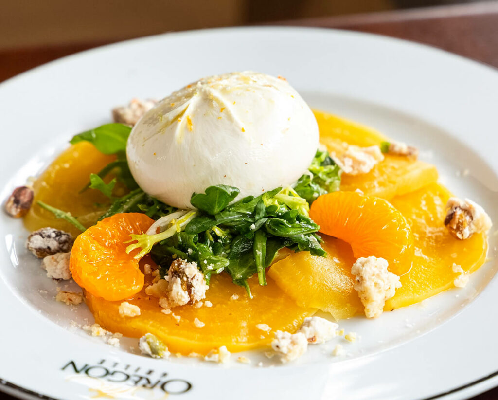 Fresh salad with burrata cheese, citrus segments, sliced mango, greens, and nuts on a white plate.