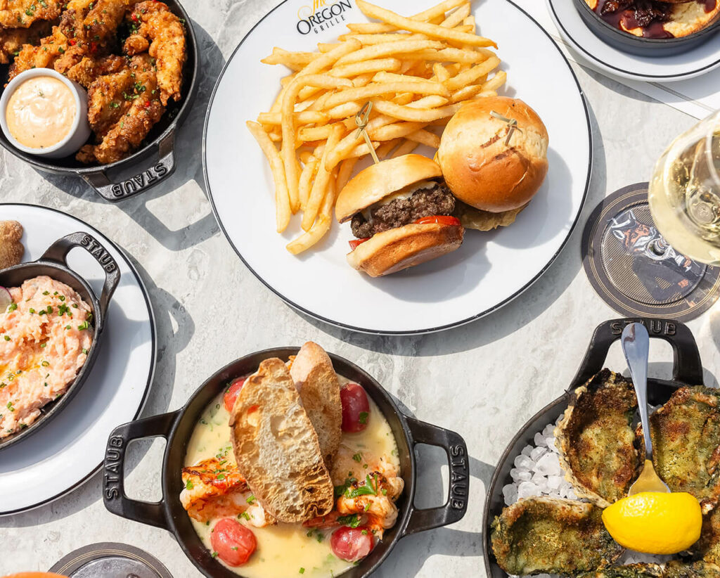 A variety of dishes including fries, a burger, shrimp, and mussels served on a sunlit table.