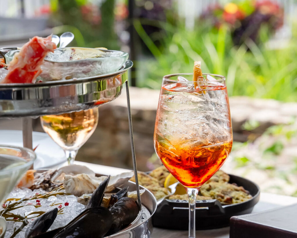 An aperol spritz served alongside a seafood platter on a sunny garden terrace.